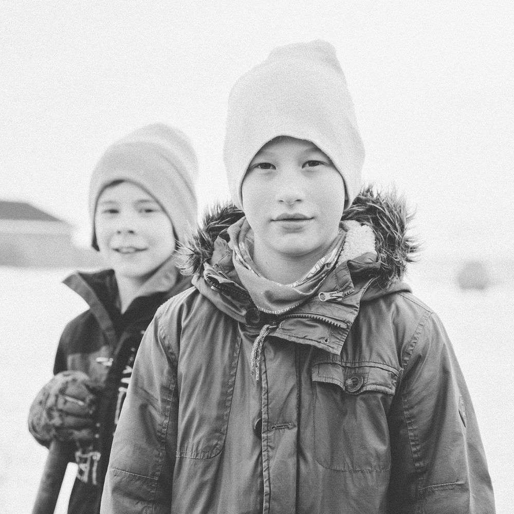 Two people wearing winter knit hats and warm coats pose together outdoors in a black and white portrait.