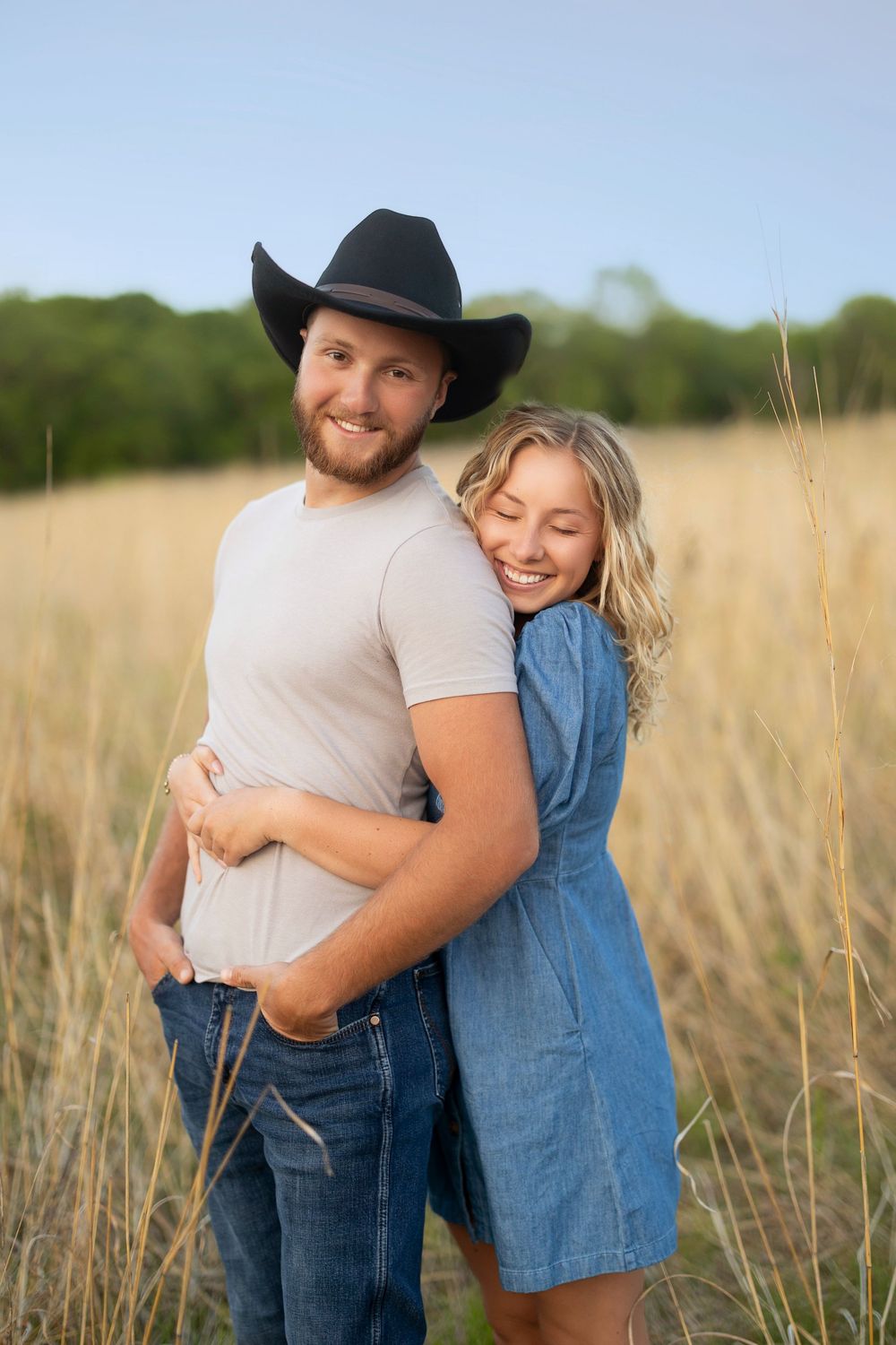 A couple embraces in a sunlit field of tall grass during a romantic outdoor photo session.
