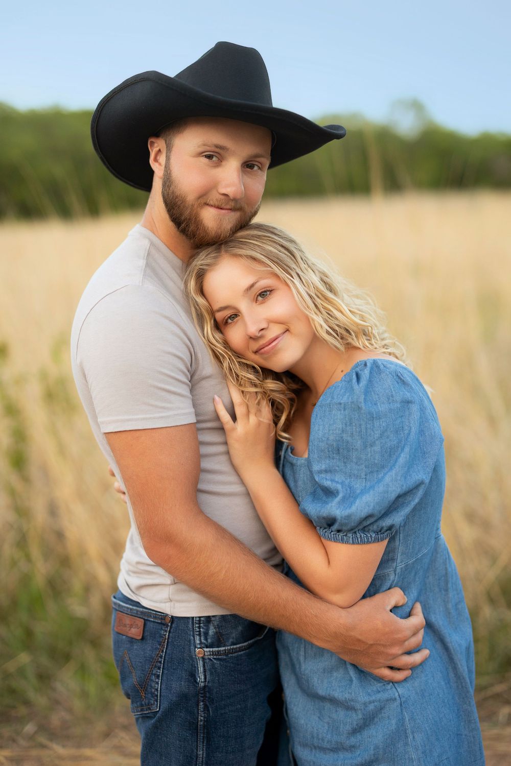A romantic countryside portrait of a couple embracing in a wheat field at sunset.