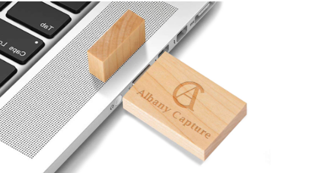 A wooden USB flash drive with engraved text plugged into a laptop keyboard's USB port.