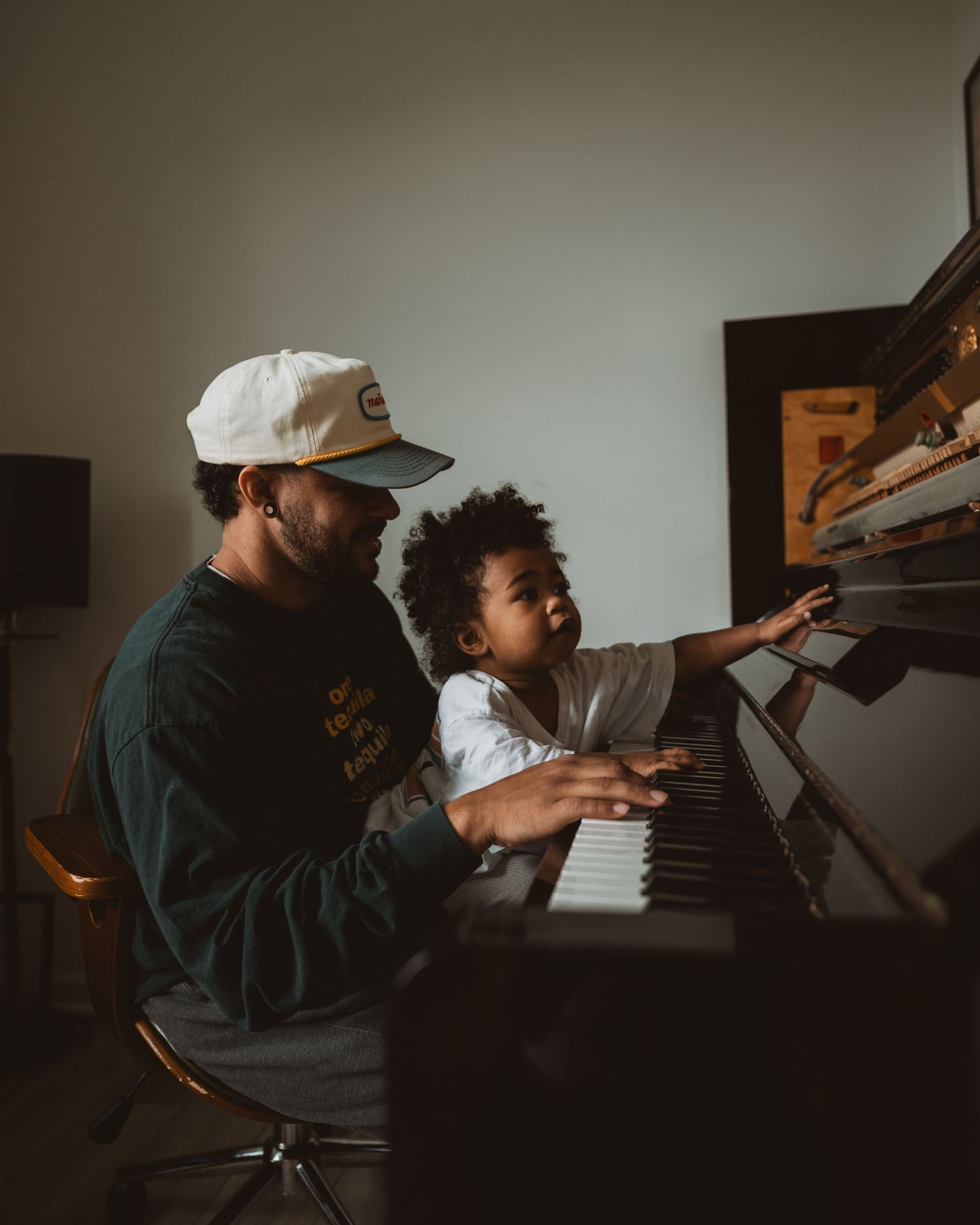 In a dimly lit room, two people share a moment at the piano, their silhouettes cast in moody lighting.