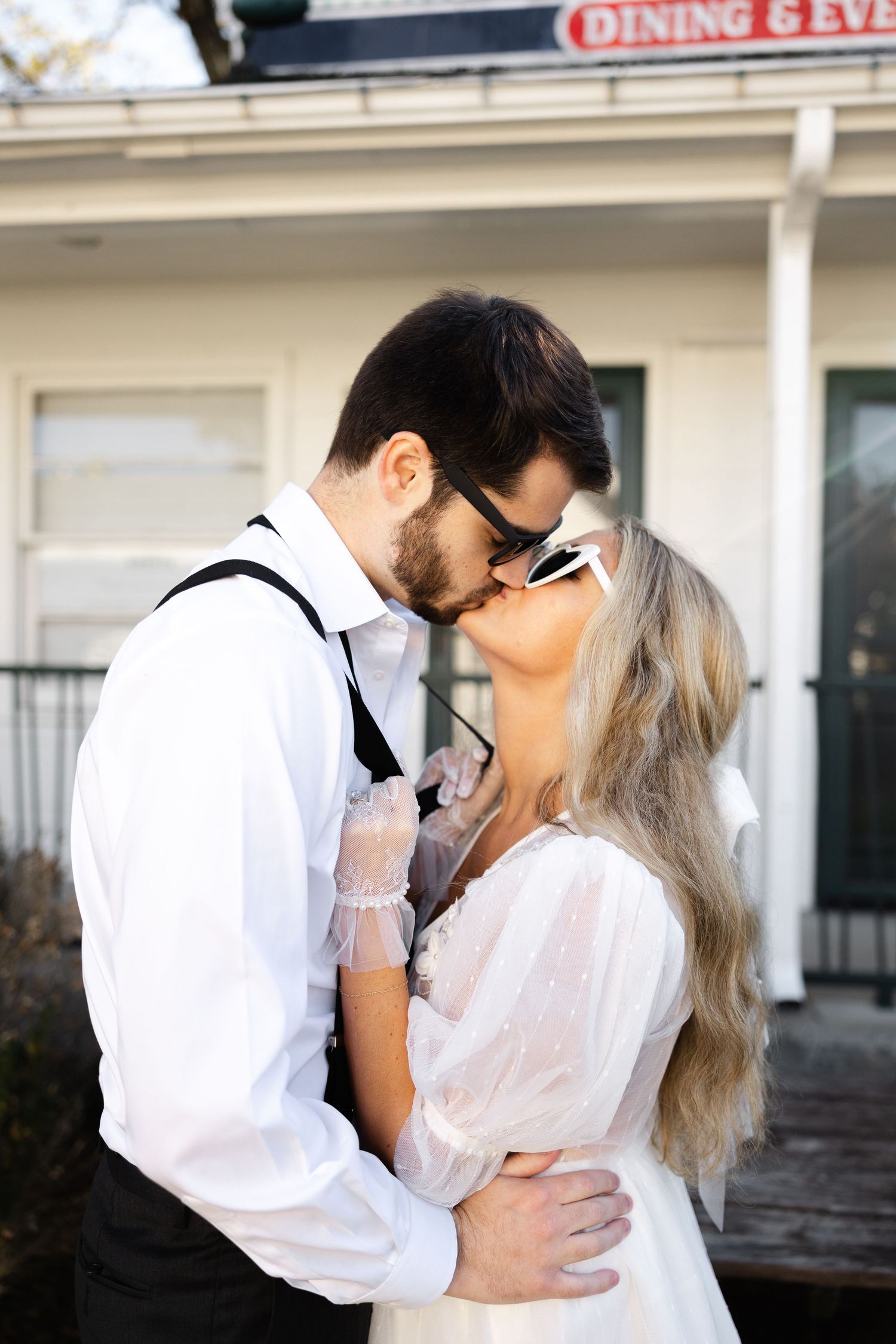 A romantic moment between a couple dressed in white as they embrace outside a rustic dining establishment.
