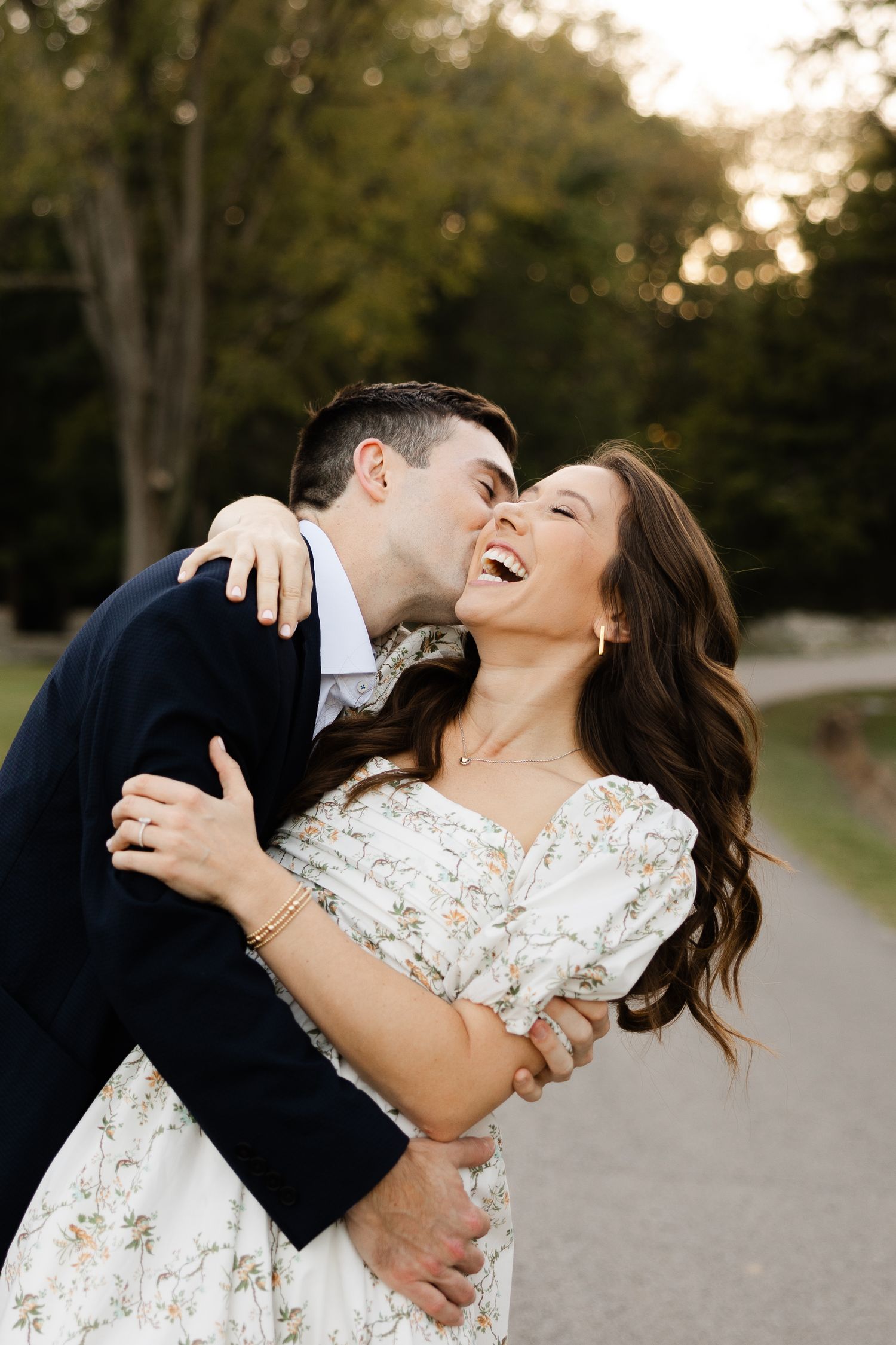 A couple shares a joyful moment of laughter during their engagement or wedding photo session on a path at sunset.