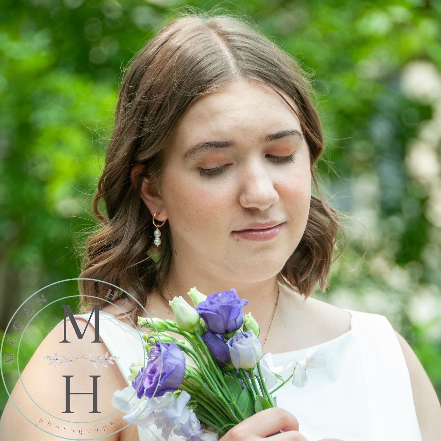 High school senior holding a bouquet of purple and white flowers against a blurred green nature background.