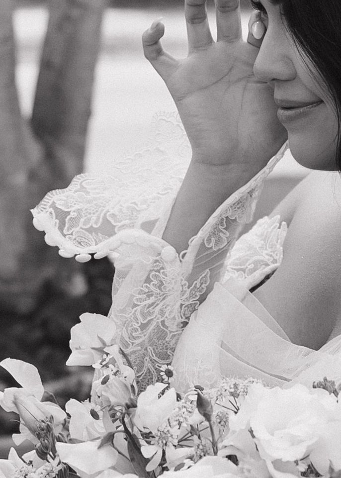 Black and white close-up of delicate lace bridal details with roses and raised hand against romantic lighting.