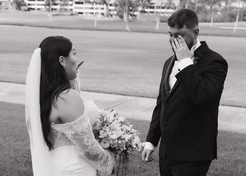 A candid black and white wedding photo captures an emotional first look moment between a bride and groom.