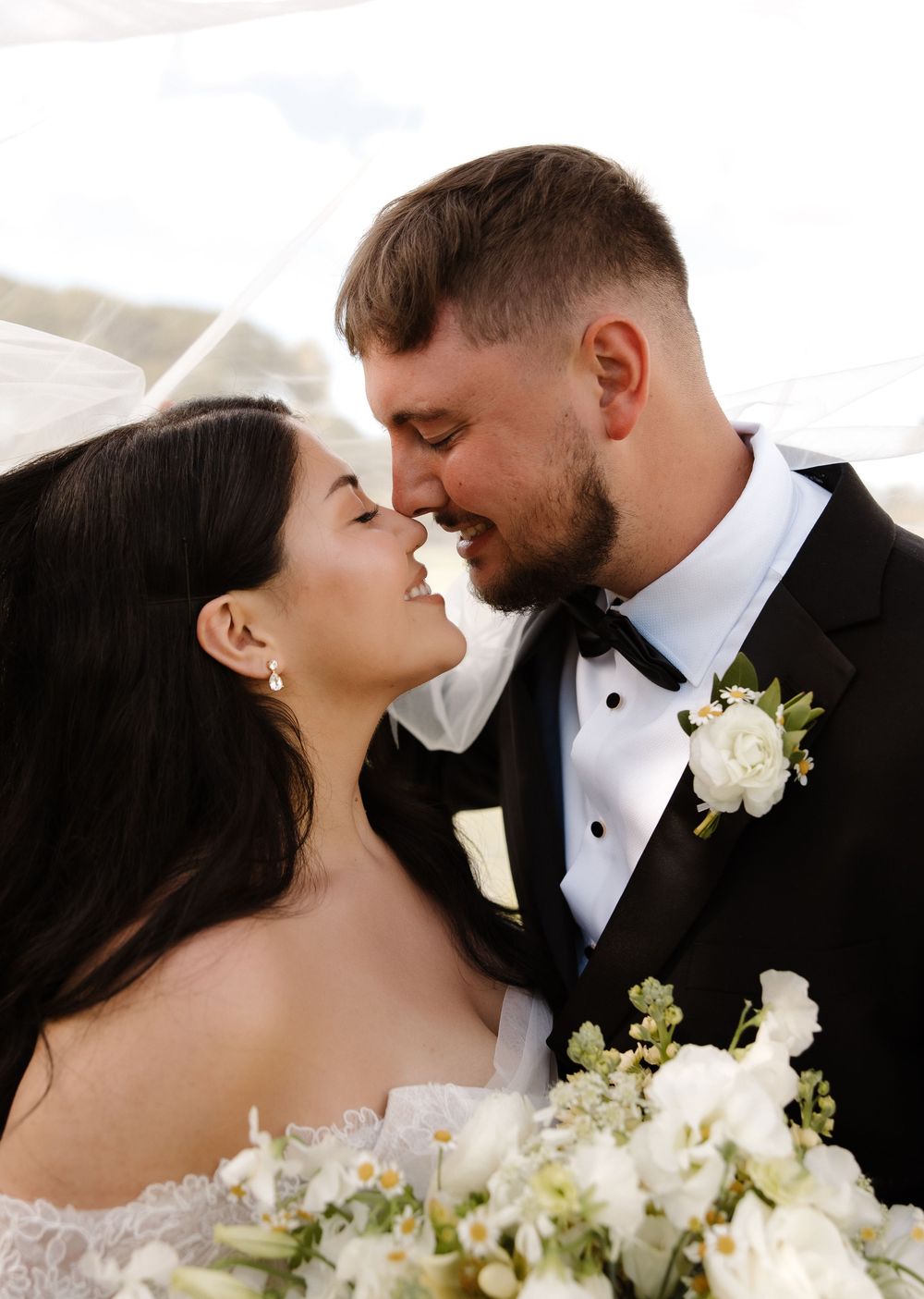 An intimate wedding portrait with white floral bouquet against warm sunlight.