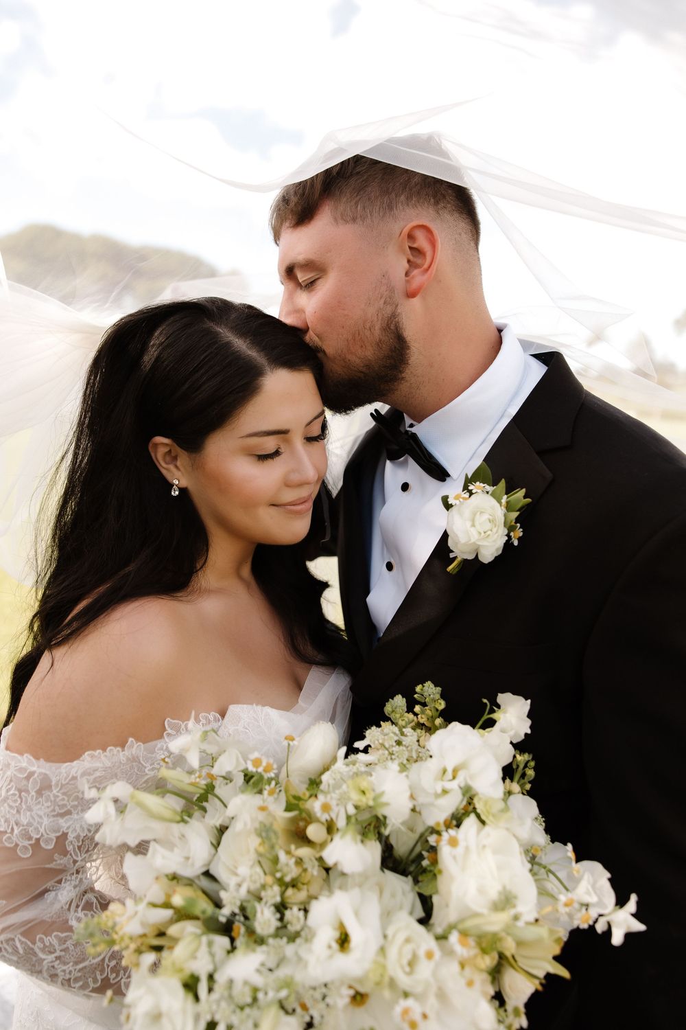 An intimate wedding portrait featuring a white floral bouquet and flowing veil.