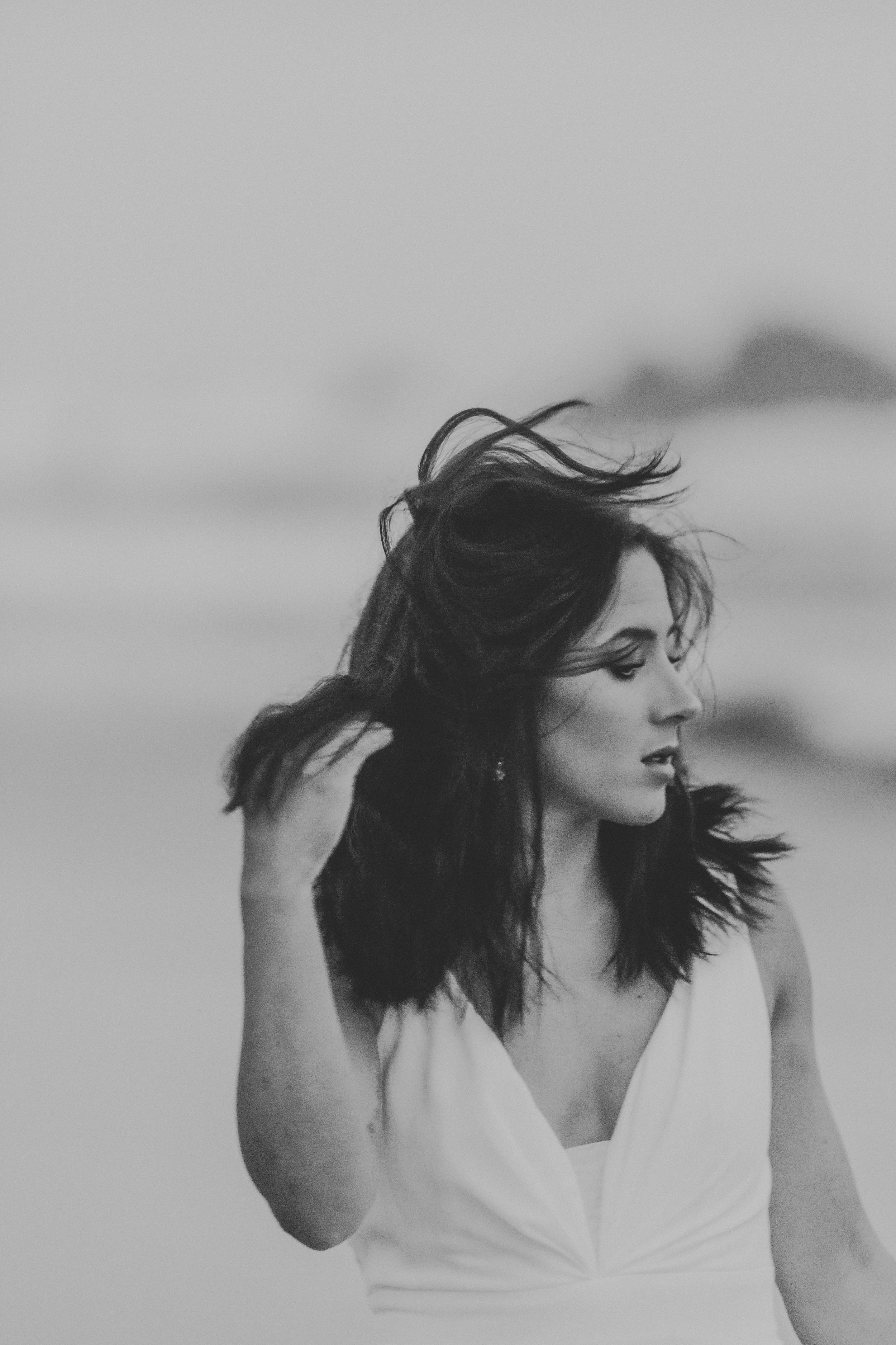 Black and white portrait of someone in white dress looking to side with windswept hair against blurred background.