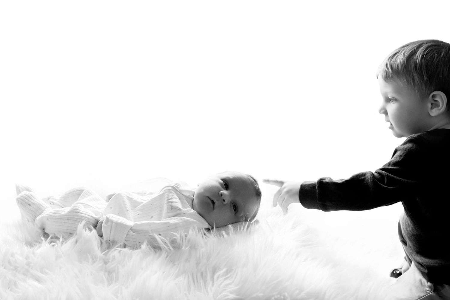 Black and white photo of two young children playing together on soft white fabric creating a dreamy atmosphere.