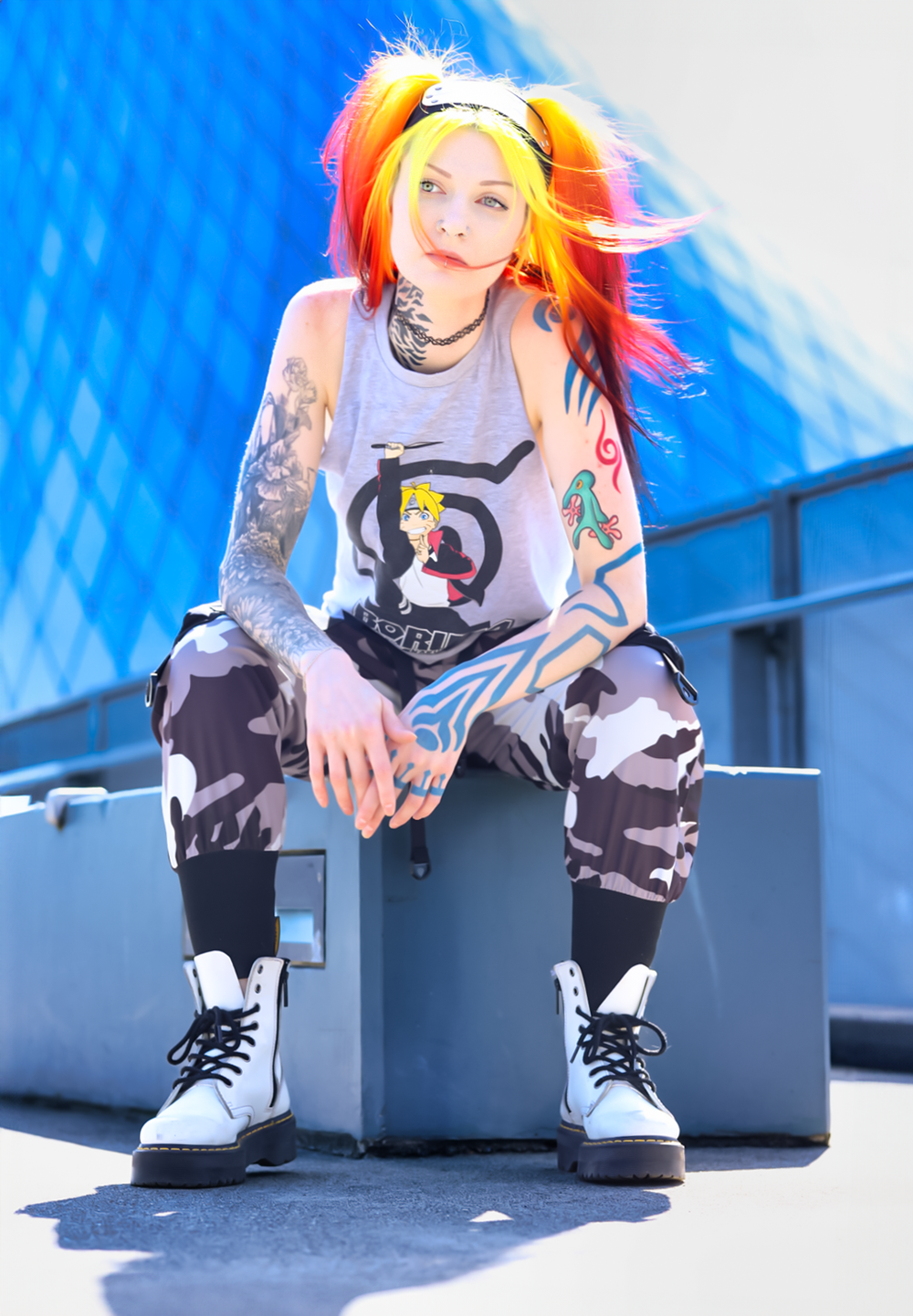 Alternative style model with colorful hair wearing camouflage pants and combat boots poses against blue background.