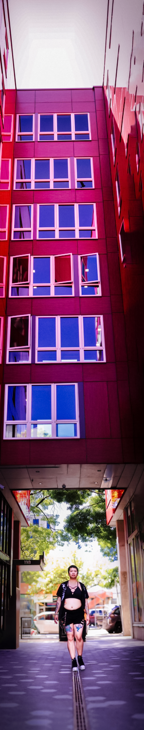 Modern urban architecture with bright red facade and blue windows above a covered walkway framed by trees.