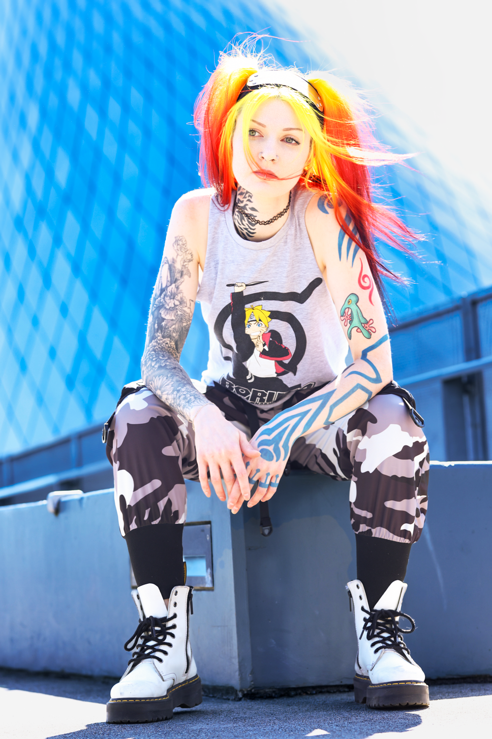 Colorful punk style outfit with bright rainbow hair, tattoos, camo pants and white boots against blue background.
