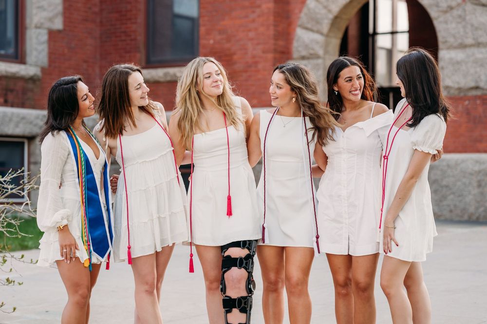 A group of six friends in white summer dresses laughing together on a city street.
