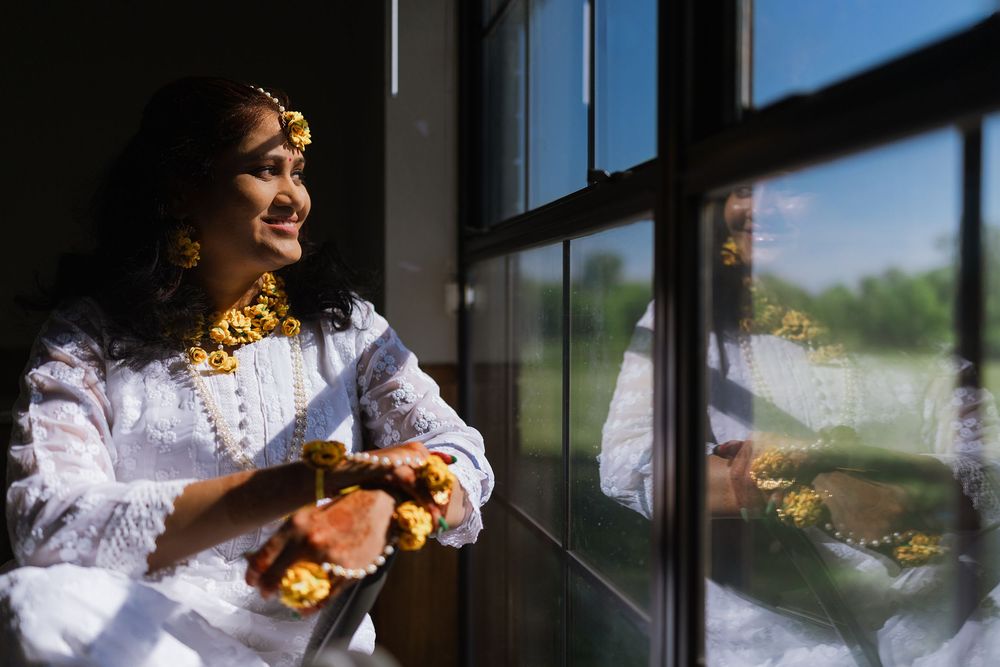 A would be Telugu bride in a white lace dress stands near a window in dramatic lighting for a portrait.