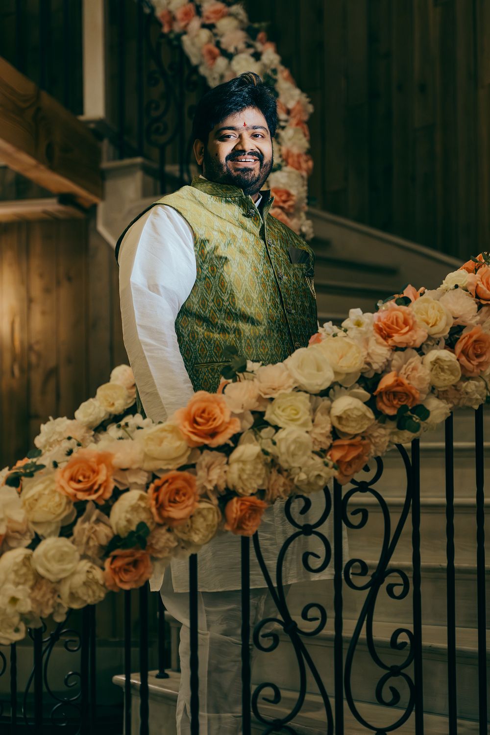 Traditional Indian wedding attire with green brocade vest shown against decorative floral staircase with peach and cream roses.