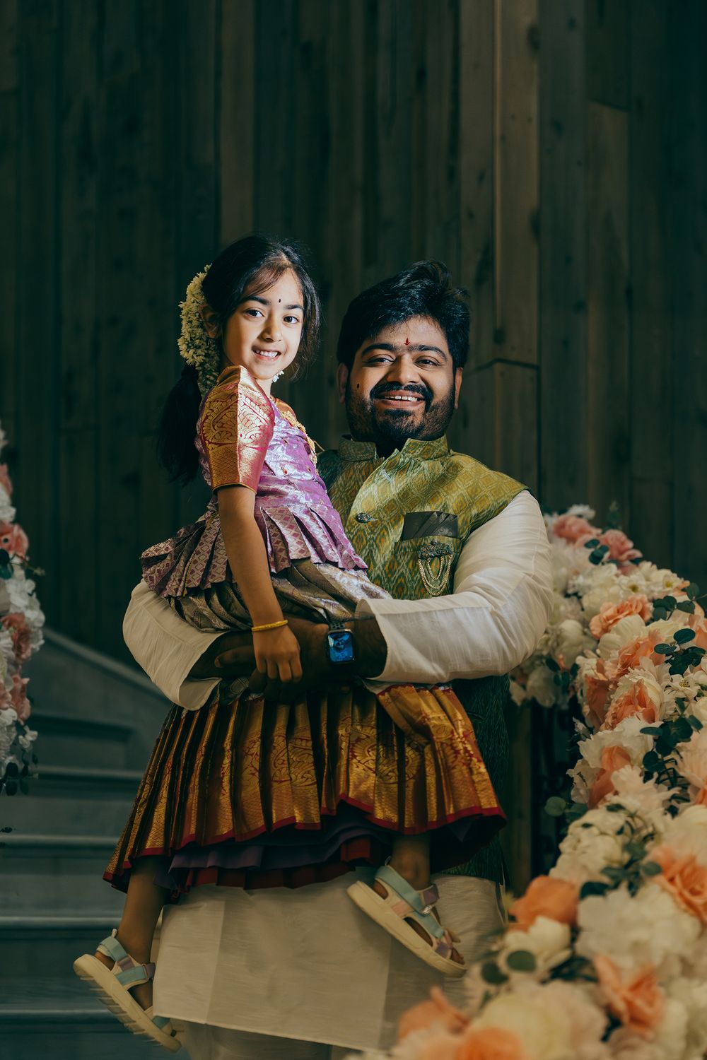 Telugu groom and niece in traditional Indian attire pose on ornate staircase decorated with peach and cream floral arrangements.