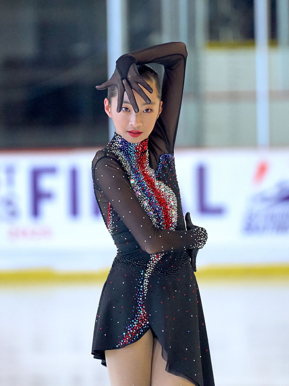 Figure skater performs graceful pose in black and red sparkly costume on ice rink during competition.