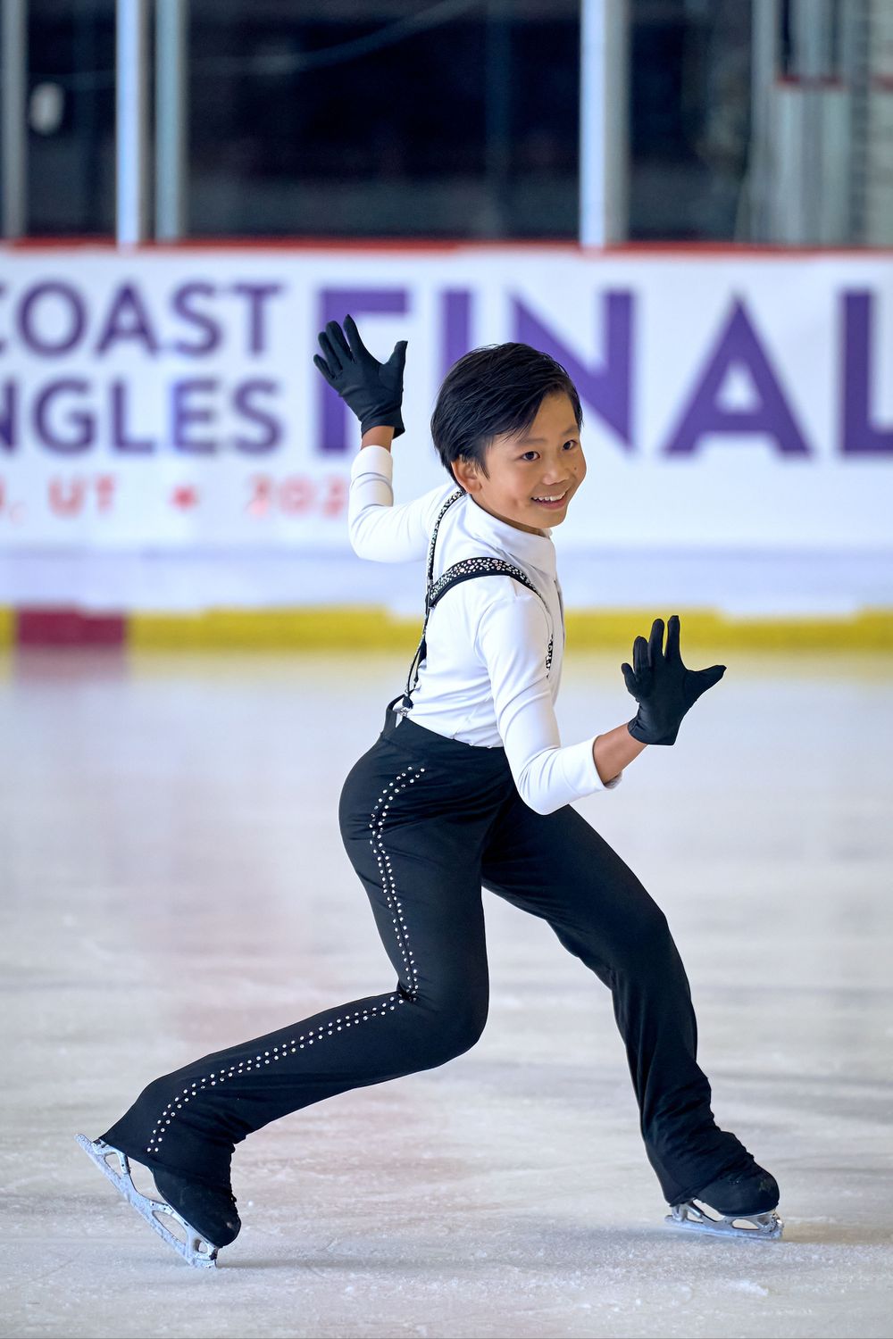 Figure skater in black and white outfit performs graceful move on ice during competition at Coast Singles event.