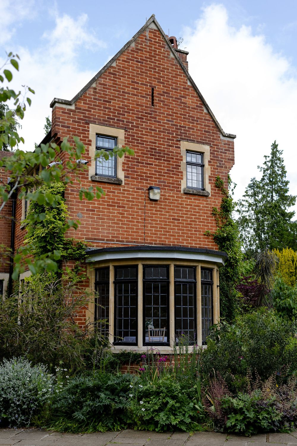 A charming red brick house with bay windows and lush garden landscaping features a curved glass conservatory entrance.