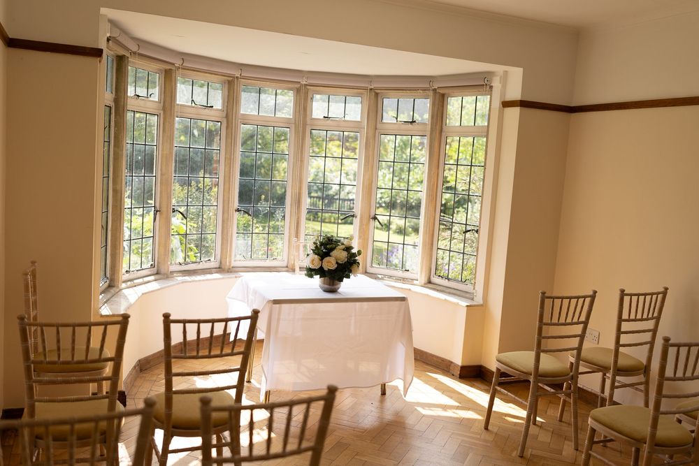 Elegant bay window dining area with hardwood floors, wooden chairs, and a white tablecloth in natural sunlight.