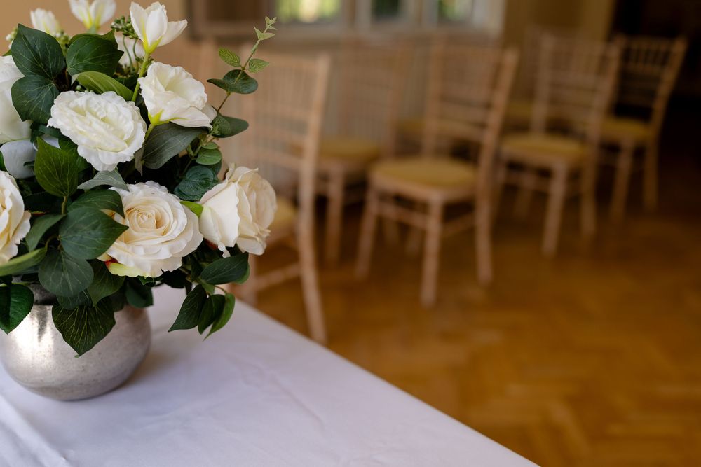 White roses in a silver vase displayed on a white tablecloth with Chiavari chairs in the background.