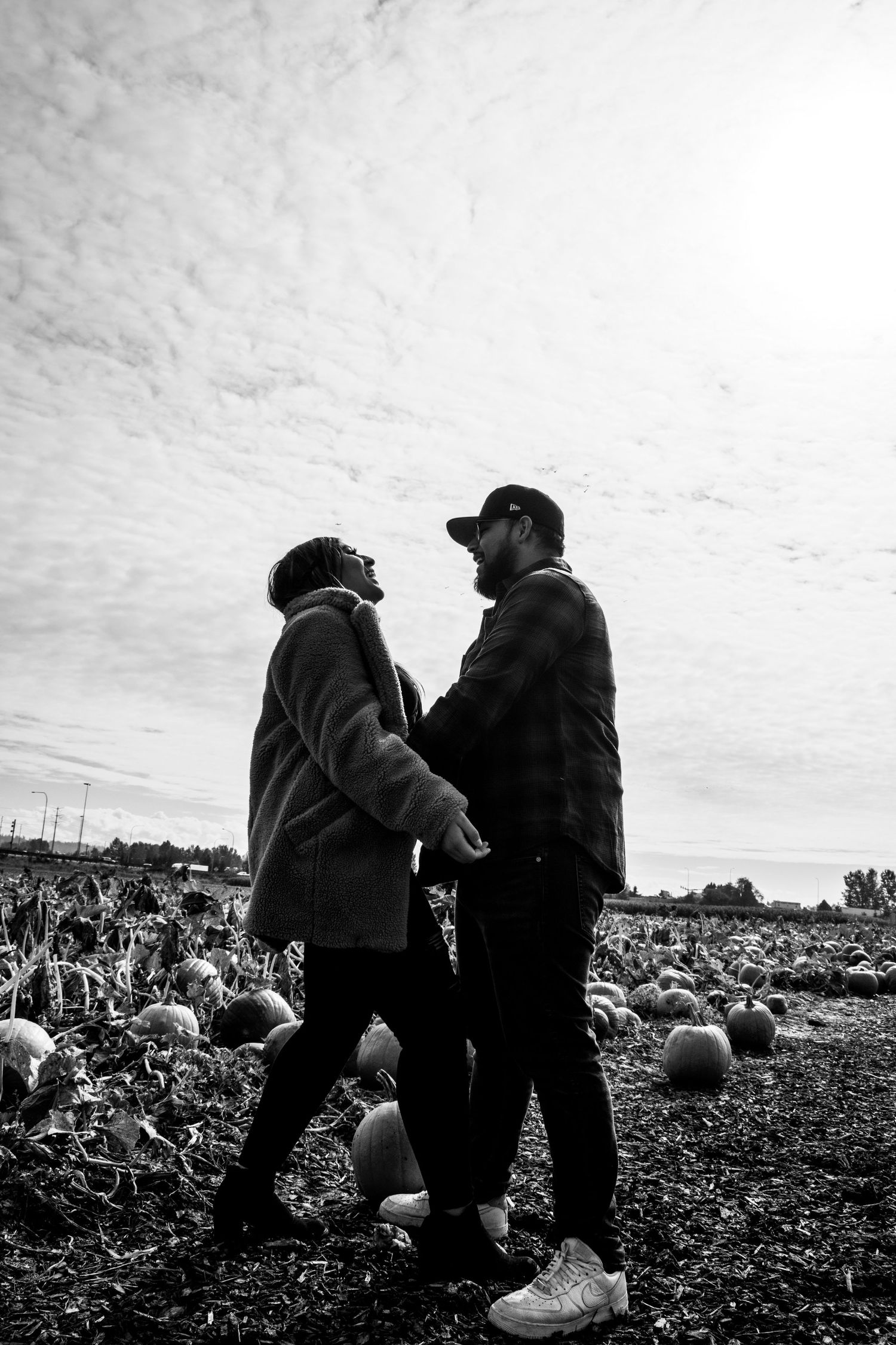 Two people looking up at cloudy sky while standing in a pumpkin field.