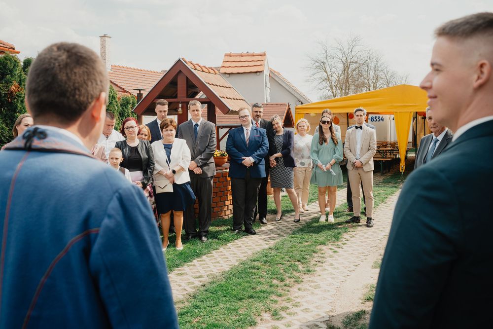 Wedding guests stand along a rustic dirt path outside a barn venue during an outdoor countryside celebration.