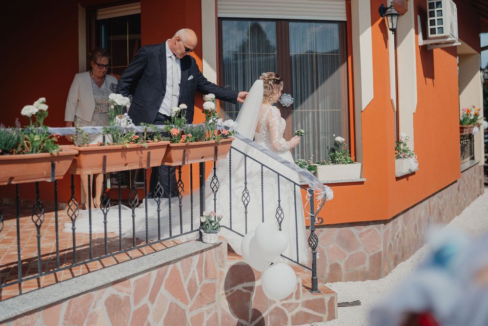 Wedding couple and guests stand on a terrace of an orange Mediterranean-style building with wrought iron railings.