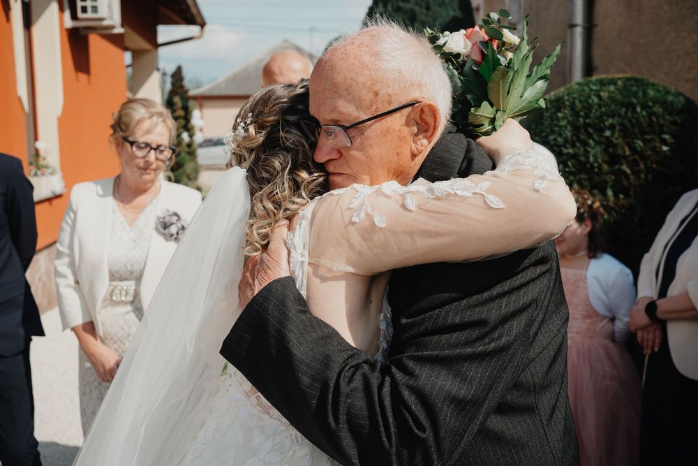 An emotional embrace at a wedding celebration as onlookers smile in the background.