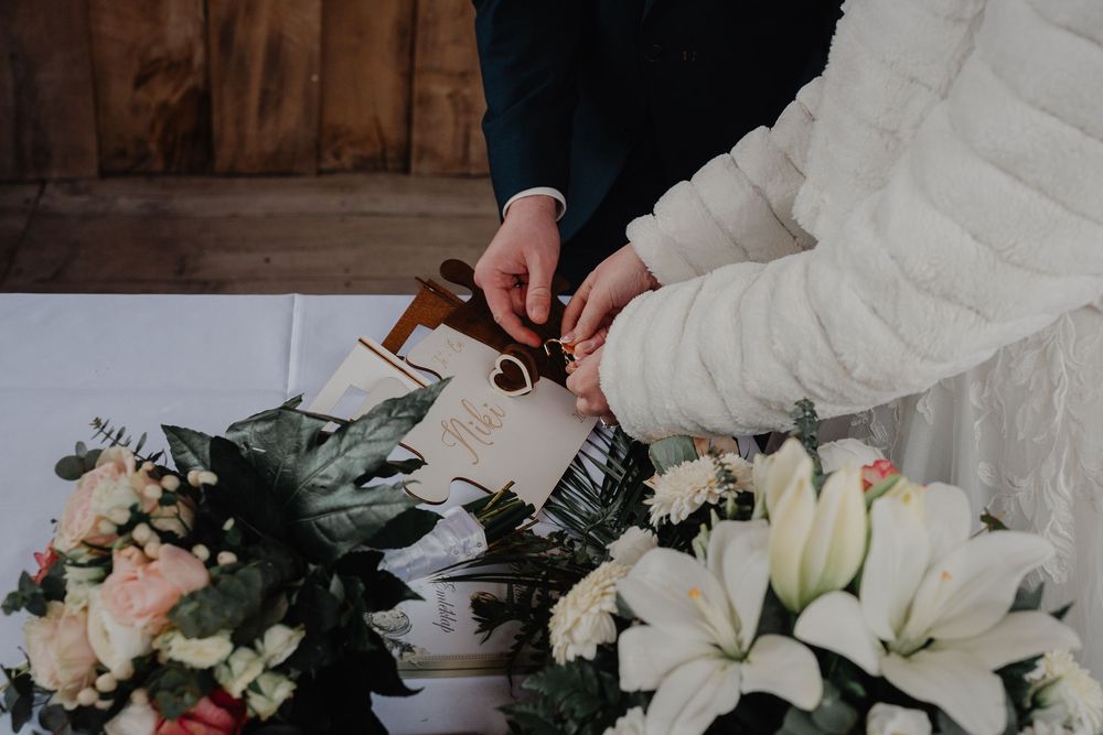 Two people sign papers on a table decorated with white lilies and blush pink floral arrangements.