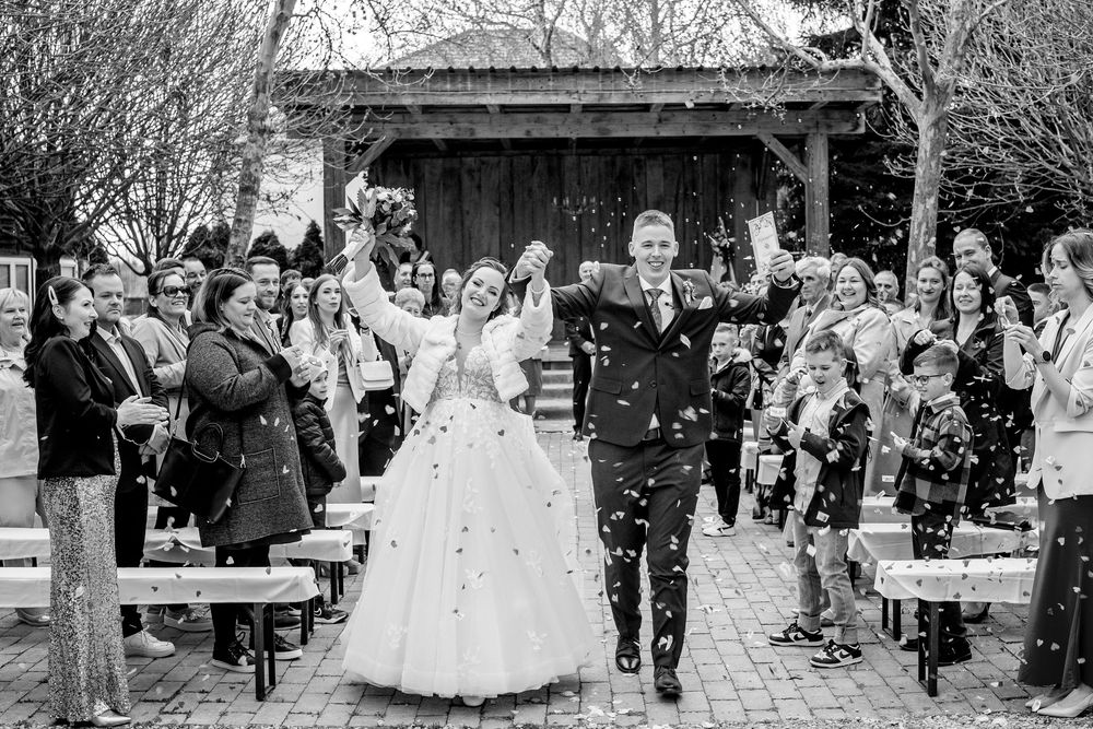 Black and white wedding photo showing newlyweds exiting ceremony while guests throw confetti along garden path.