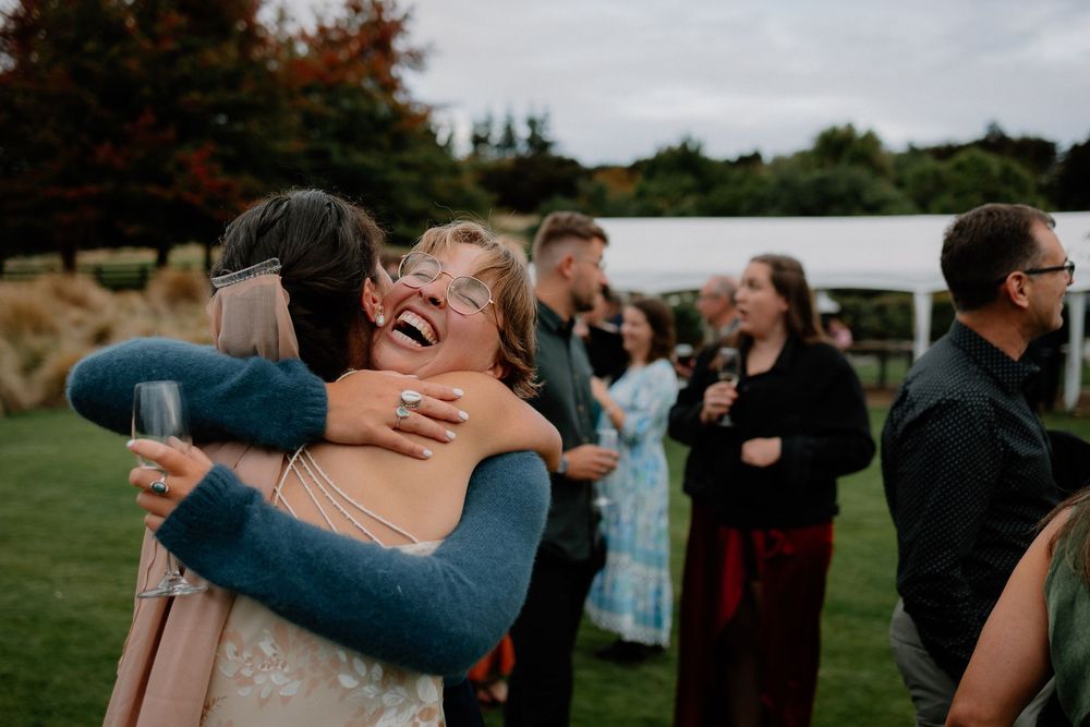Heartfelt embrace shared between guests during outdoor celebration with autumn foliage in background.