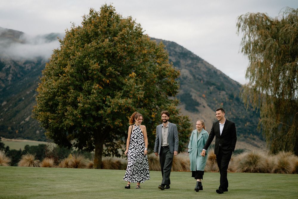 Group walking together on a grassy lawn with mountains and a large tree in the background on a misty day.