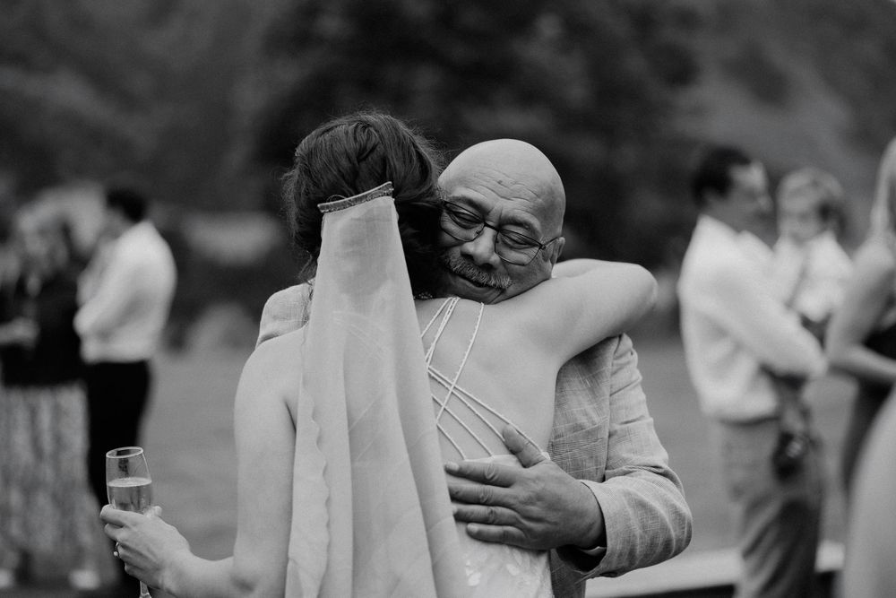 Two people share a warm embrace at an outdoor celebration while holding drinks in their hands.