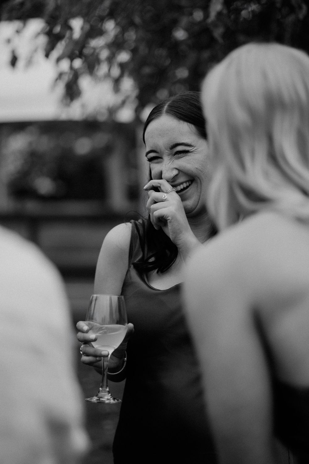 A candid black and white image capturing a joyful moment of laughter during a social gathering with wine.