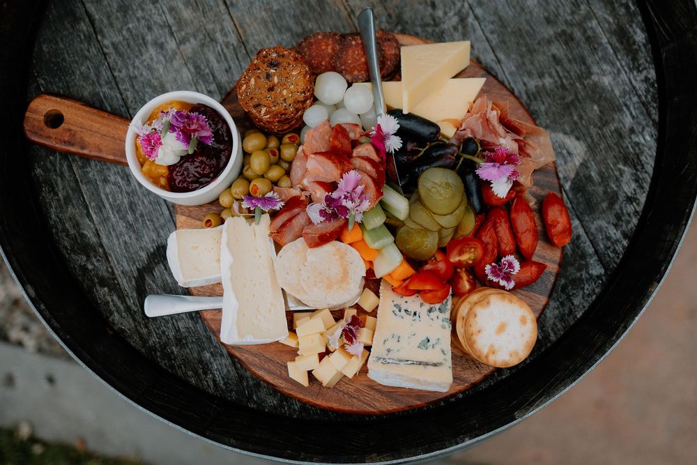 An overhead view of a gourmet charcuterie board with meats, cheeses, fruits, nuts and pickled vegetables on dark stone.