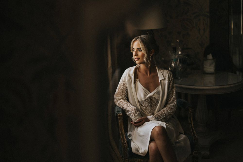 Silhouette of woman in white robe sitting by window with dramatic natural lighting in dark moody setting.