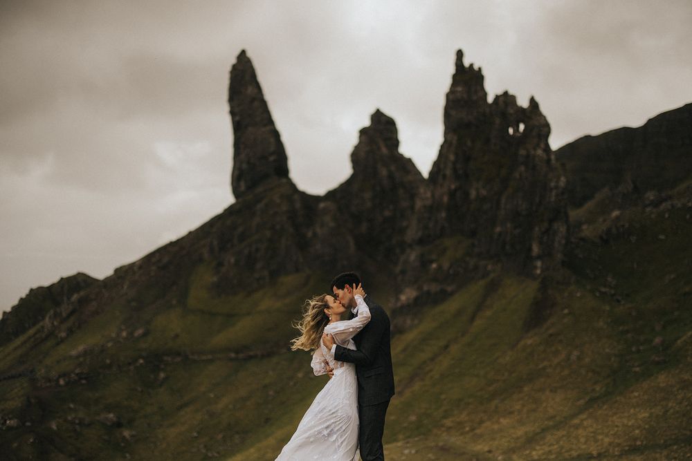 A wedding couple walks hand in hand near the dramatic rocky cliffs of the Isle of Skye in Scotland.
