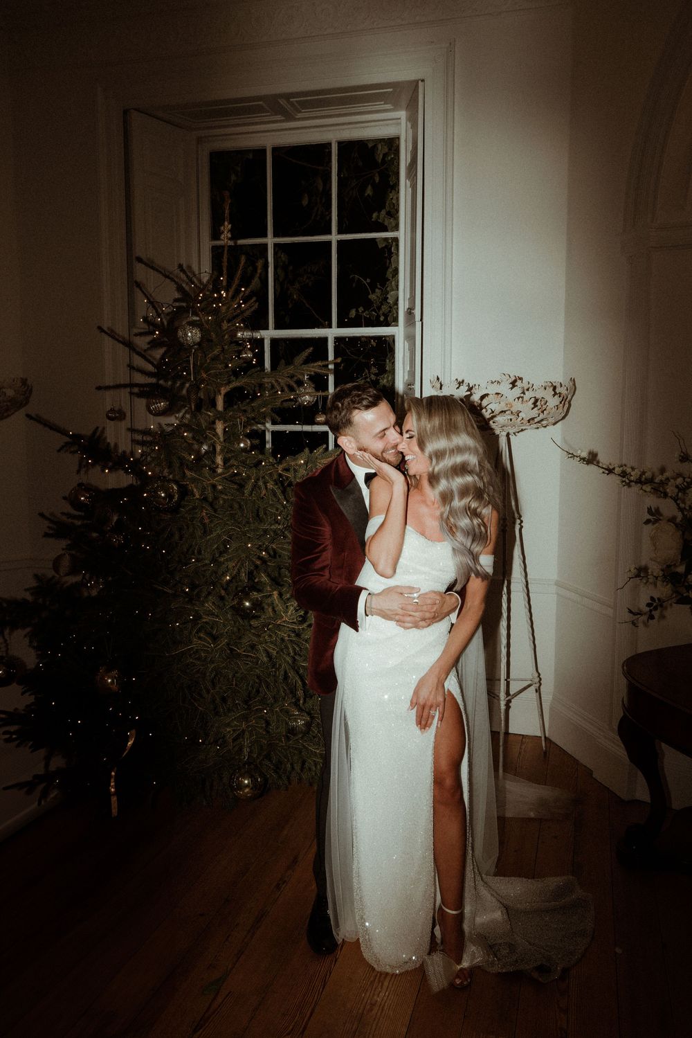 A romantic moment at a holiday party with a Christmas tree in the background, set in an elegant room with hardwood floors.