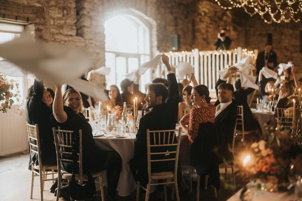 Wedding guests dining in a rustic stone venue with string lights and elegant table settings during an evening reception.