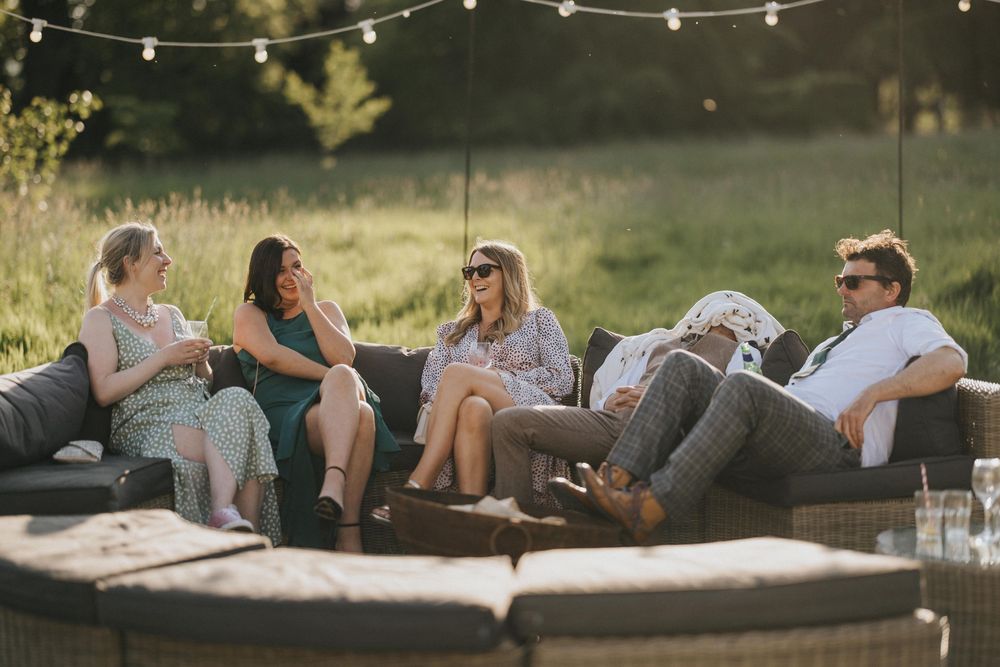 String lights illuminate outdoor seating around a circular fire pit with cushioned lounge chairs on a warm evening.
