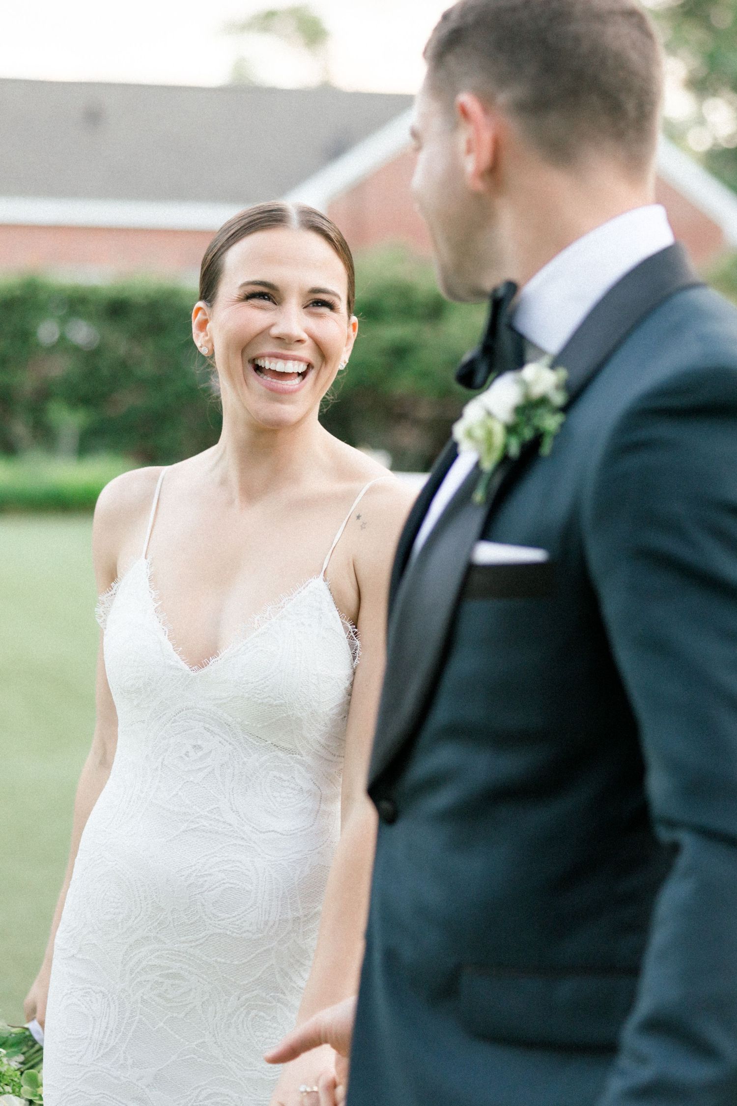 A bride in a sleeveless lace dress shares a joyful moment with her groom outdoors during their wedding celebration.