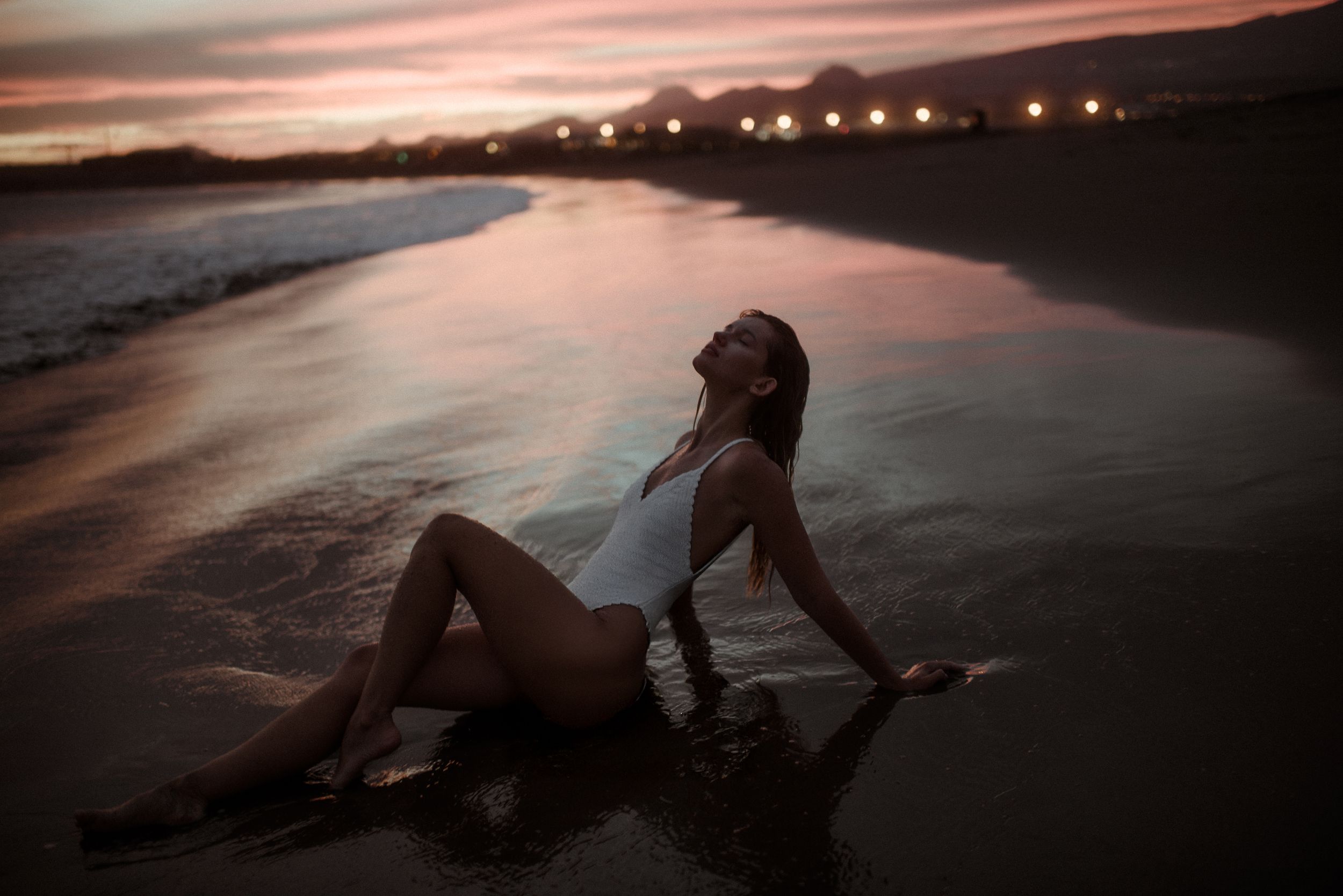 A woman posing at La Tejita beach at sunset with moody pink sky and calm waters. Portrait photoshoot in Tenerife.