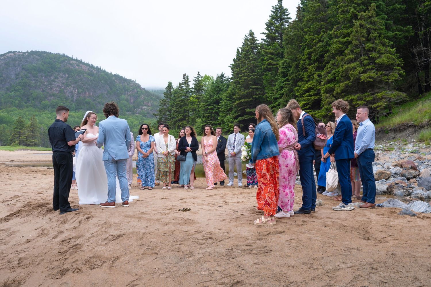 A romantic beach wedding ceremony takes place on a sandy shoreline with cloudy skies and ocean waves in the background