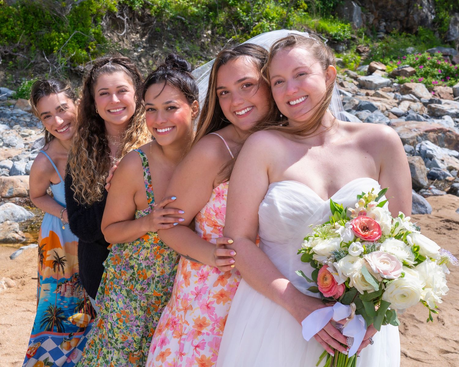 Group photo of smiling bridesmaids wearing colorful floral dresses posing together outdoors in Bar Harbor, Maine.