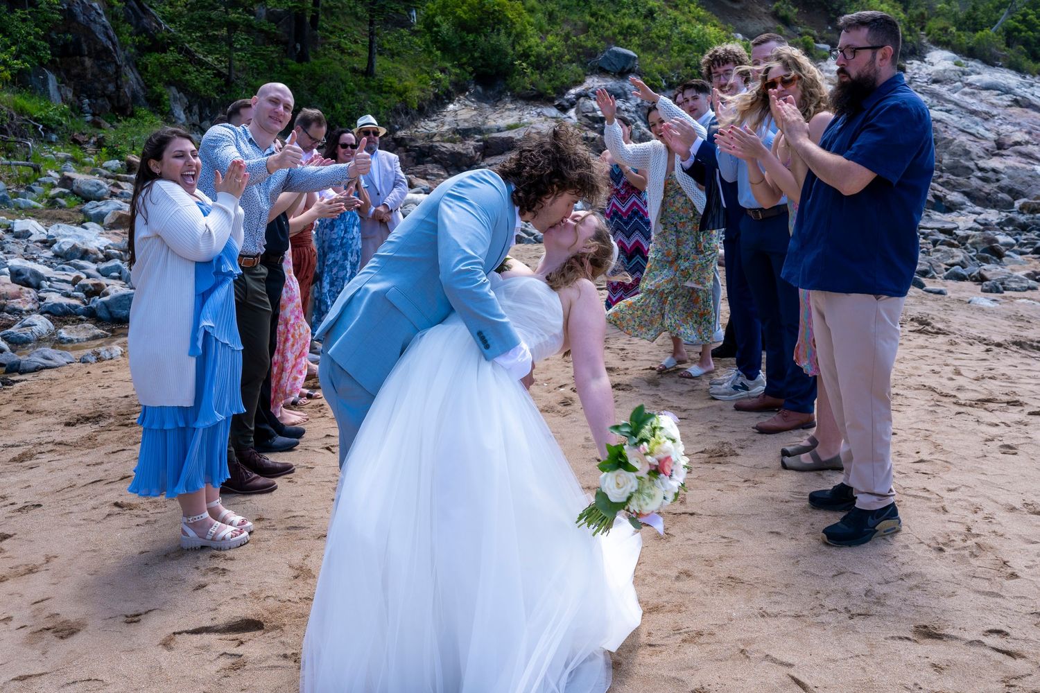 Seaside wedding ceremony on a sandy beach with guests in blue and white attire documenting the special moment.