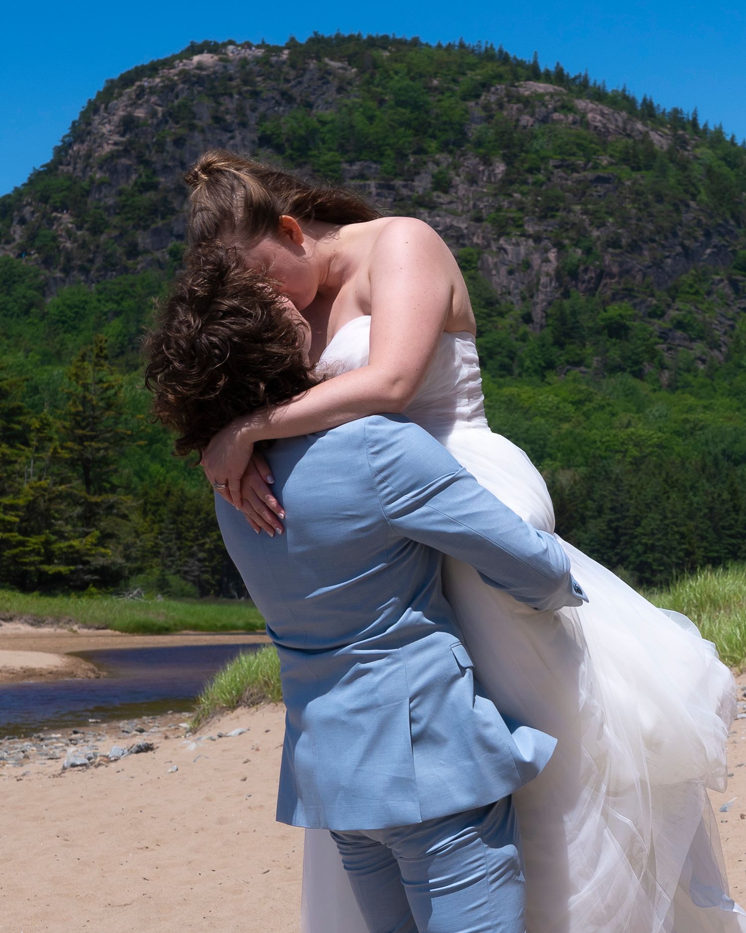 A couple embraces in an intimate romantic moment on a beach with a majestic mountain landscape in the background.