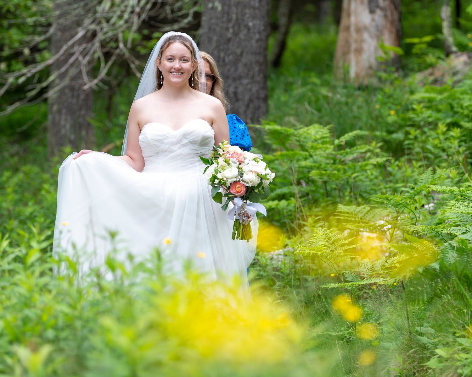 A wedding portrait in a lush green forest garden with vibrant yellow wildflowers in the foreground.