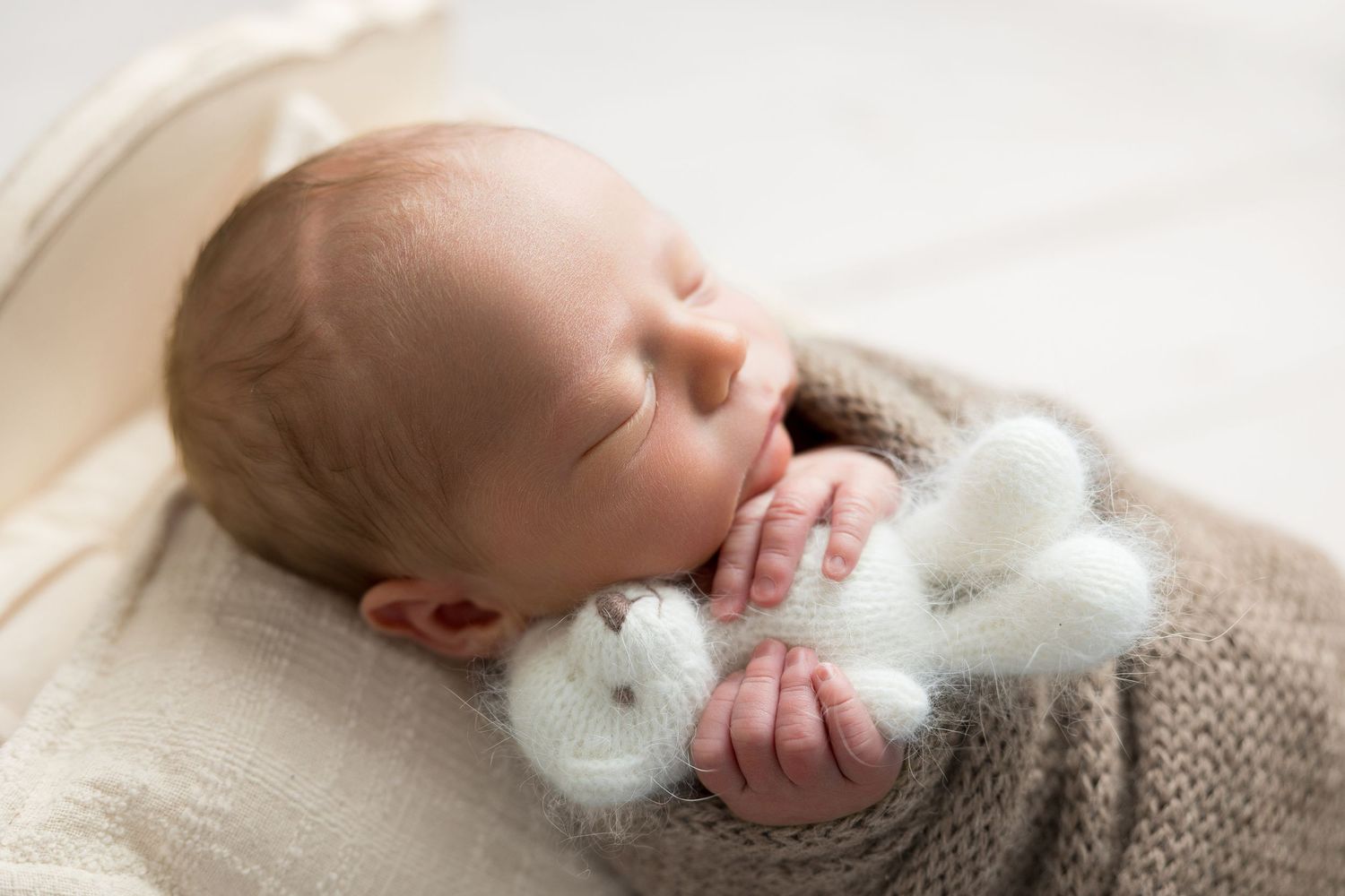 Peaceful sleeping newborn wrapped in cozy yellow knit blanket rests in wooden basket.